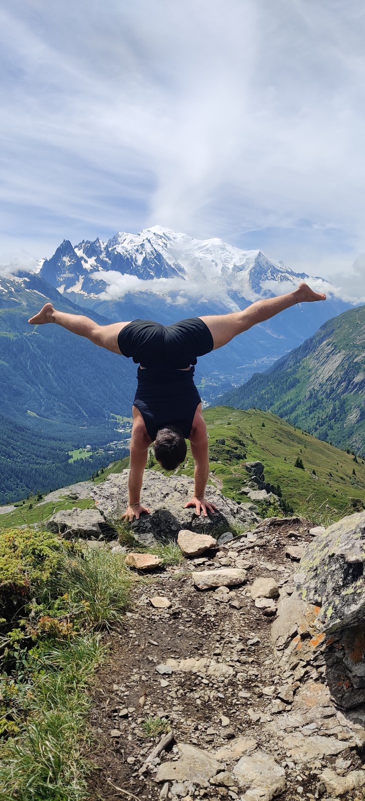 Wolf Bogaert in a straddle handstand on a rock with the snow-capped Mont Blanc behind